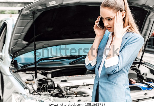 Woman calling for assistance with broken down car\
engine on street