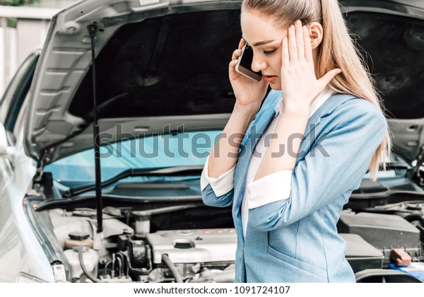 Woman calling for assistance with broken down car\
engine on street