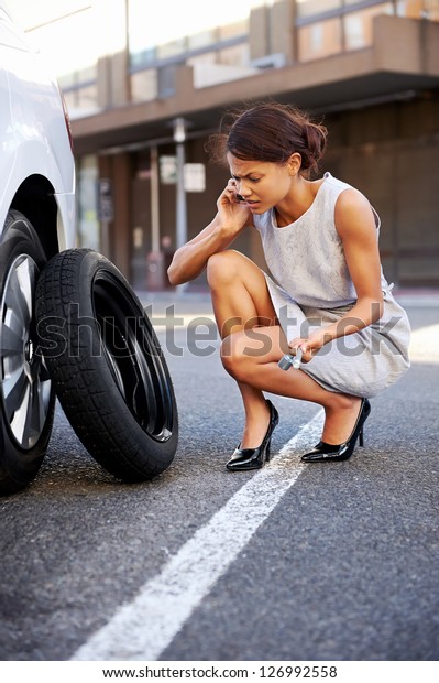 Woman calling for assistance with flat tire on car\
in the city
