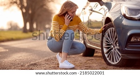 Woman Calling For Help On Phone After Car Breakdown On Country Road With Tyre Puncture