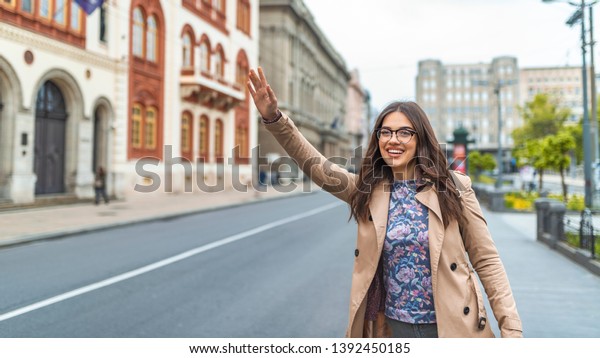 Woman calling a taxi.\
Concept about urban life, people and transportation.  Young smiling\
american woman catching taxi at city street. Woman looking for a\
taxi