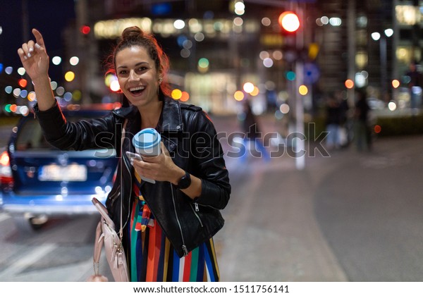 Woman calling taxi\
on city street at night\
