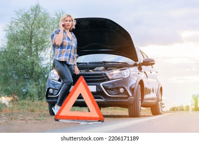 A Woman Calls The Service Department Standing At The Open Hood Of The Car, An Emergency Stop Sign