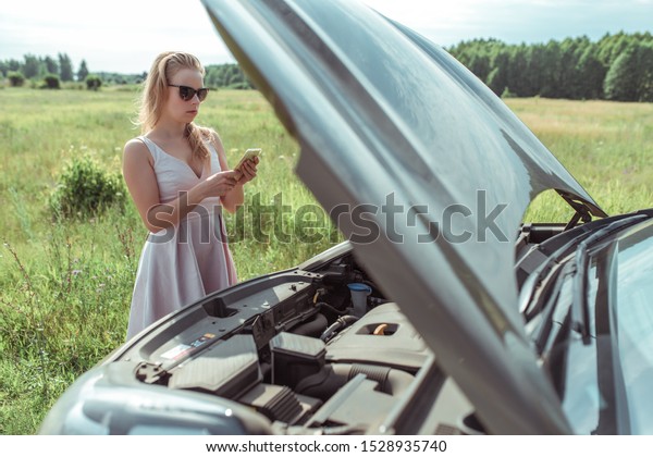 woman calls, writes reads message,\
summer road, car broke down, an open hood, an accident, an\
emergency call, tow truck in the country. Pink dress\
sunglasses.