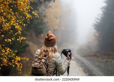 Woman with camera and backpack hiking in misty autumn forest. female tourist photographing nature - Powered by Shutterstock