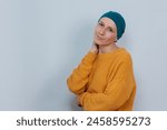 A woman cancer survivor wear a hat with serene expression a white wall in the background