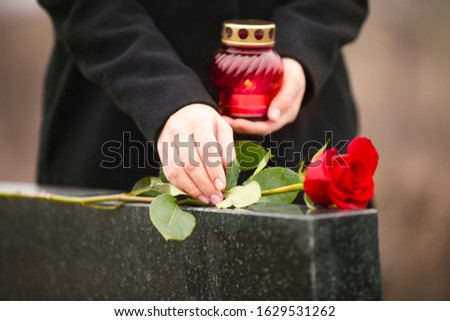 Woman with candle near black granite tombstone outdoors, focus on red rose. Funeral ceremony