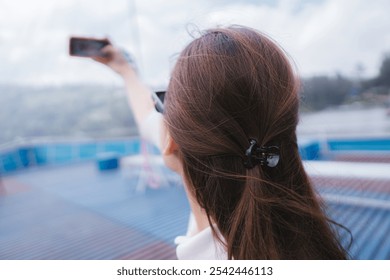 A woman captures a selfie while outdoors, her back to the camera, holding her phone at arm's length - Powered by Shutterstock