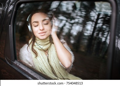 Woman In The Car, Autumn Concept. Smiling Pretty Girl Listening To Music On Your Smartphone With Headphones Moving In Car