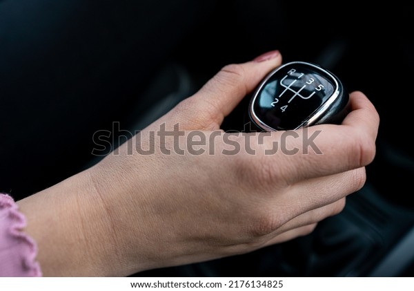 Woman in a car cockpit shifting a speed and using\
a hand brake.
