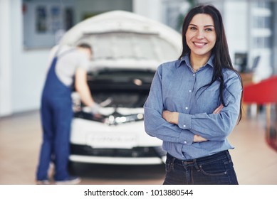 Woman at a car garage getting mechanical service. The mechanic works under the hood of the car. - Powered by Shutterstock