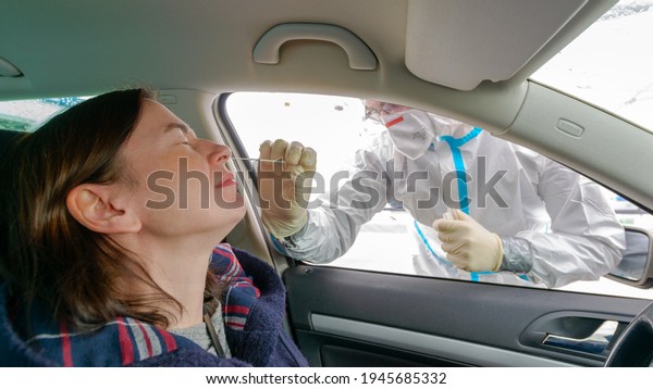 Woman in a car getting a\
nasal swab test. Doctor or nurse wearing PPE, N95 mask, face shield\
and personal protective apron, standing next to car - Covid-19\
screening