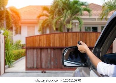 Woman in car, hand holding and using remote control to open or close the auto wooden gate when drive and arrived home.  Security and save time concept.