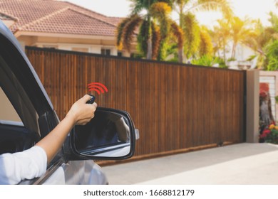 Woman In Car, Hand Holding And Using Remote Control To Open The Electric Sliding Auto Wooden Door. Home Remote Control, Auto Garage, Automatic Gate And Security System In Concept. 