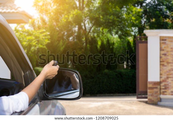 Woman in car, hand holding and using remote\
control to open the auto gate when driving and arrive home.\
Security system and save time\
concept.
