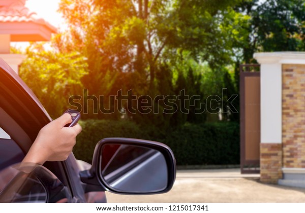 Woman in car, hand holding and using remote\
control to open the auto gate when driving and arrive home.\
Security system and save time\
concept.