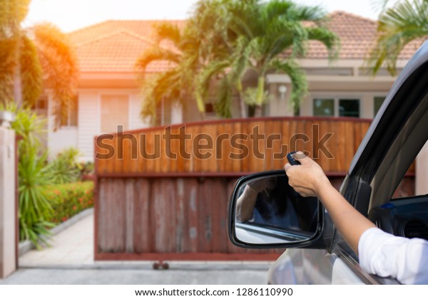 Woman in car, hand holding and using remote\
control to open or close the auto wooden gate when drive and\
arrived home.  Security and save time\
concept.