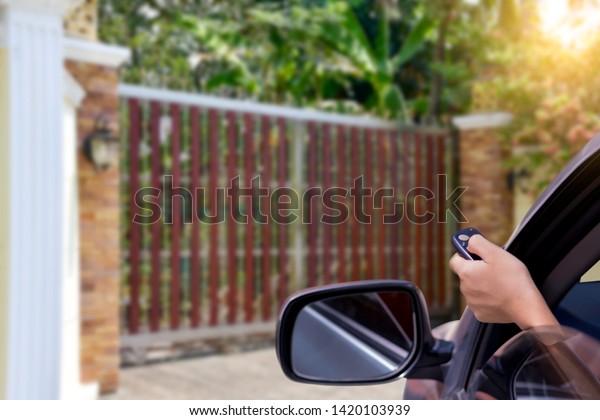 Woman in car, hand opening the automatic gate by\
using remote control while driving arrived home .Home security\
system and save time\
concept.