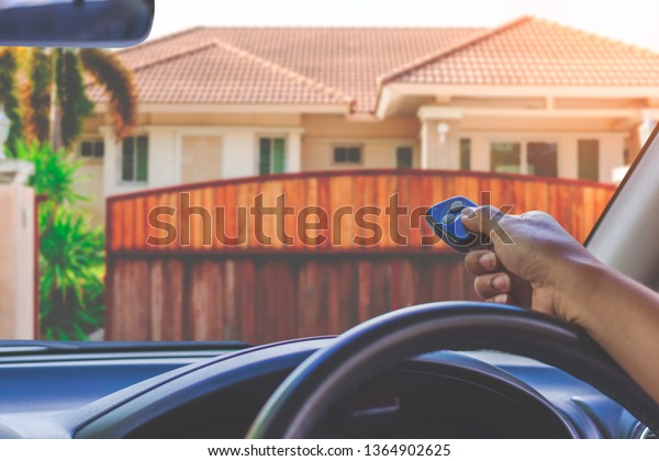 Woman in car, hand
using remote control to open the wooden automatic gate with modern 
home blurred background when  arrived home. Home remote control
auto door in concept.