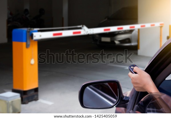 Woman in car, hand using remote control to open\
the automatic barrier of the car parking .Home security system and\
save time concept.