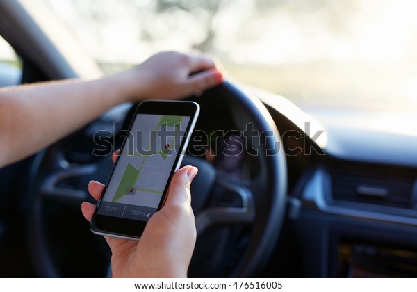Woman in the car and holding black\
mobile phone with map gps navigation, toned at\
sunset.