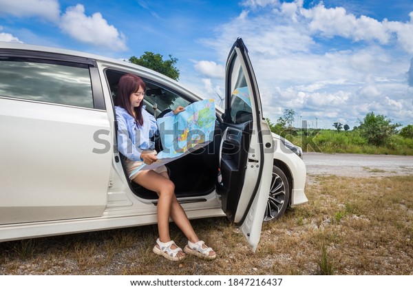 woman in a car looking at a map to\
reach the holiday destination with blue sky\
background