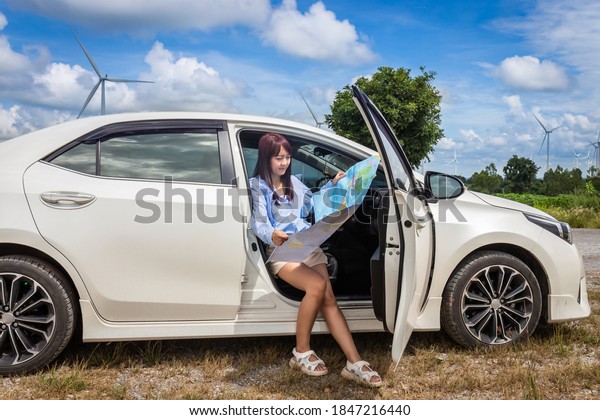 woman in a car\
looking at a map to reach the holiday destination with blue sky and\
wind turbines background