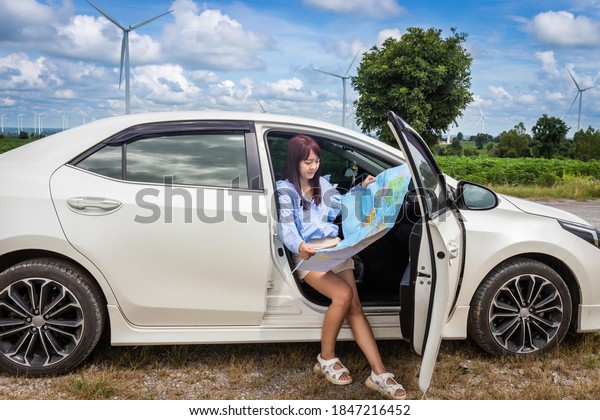 woman in a car\
looking at a map to reach the holiday destination with blue sky and\
wind turbines background