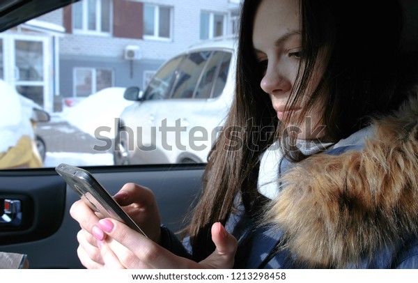 Woman in a car\
with a mobile phone. Young beautiful brunette woman looking\
something in the mobile\
phone.