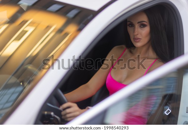 A\
woman in car, selects navigation application on touch screen\
display. pink dress. automatic gearbox, in parking lot near\
shopping center, car interior, radio station\
selection.