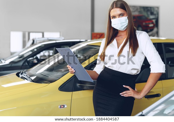 Woman car seller standing near new car wearing\
protective face mask