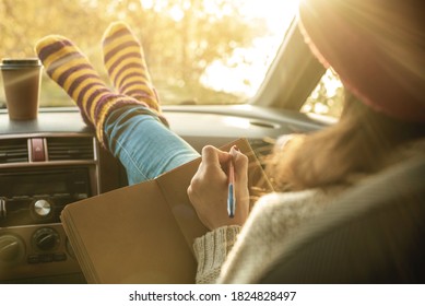 Woman In A Car In Warm Socks Is Writing Notes And Plans In A Notebook. Cozy Autumn Weekend Trip. The Concept Of Freedom Of Travel