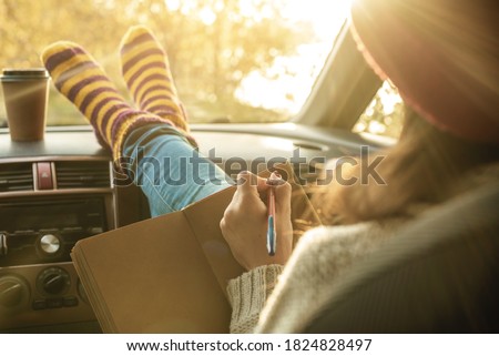 Woman in a car in warm socks is writing notes and plans in a notebook. Cozy autumn weekend trip. The concept of freedom of travel
