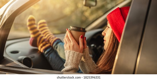 Woman in a car in warm woolen socks yellow is holding a Cup of coffee in hands at sunset. Cozy autumn weekend trip. The concept of freedom of travel - Powered by Shutterstock