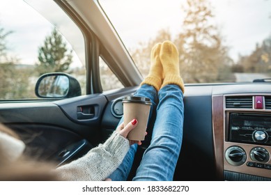 Woman in a car in warm woolen yellow socks is holding a Cup of coffee in hands. Cozy autumn weekend trip. The concept of freedom of travel - Shutterstock ID 1833682270