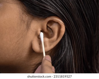 The woman carefully cleans her ear with an earbud, ensuring personal hygiene and maintaining ear health with gentle precision. - Shutterstock ID 2311819527
