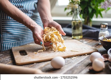 Woman is carefully holding raw fresh homemade noodles in her hands. Concept of process of cooking handmade pasta in a cozy atmosphere