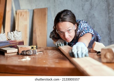 Woman carpenter checking quality of a plank for project. Hardworking middle aged female worker looking and choosing wood in the woodshop or garage.