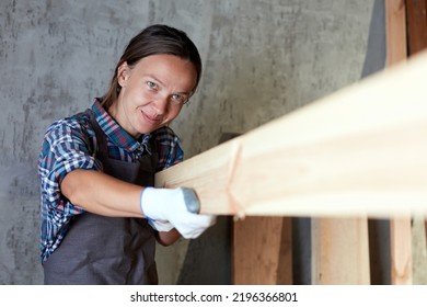 Woman Carpenter Checking Quality Of A Plank For Project. Hardworking Middle Aged Female Worker Looking And Choosing Wood In The Woodshop Or Garage.