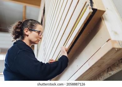 Woman Carpenter Measuring Up A Prefabricated Section Of Timber Wall In A Factory During A Quality Control Inspection In A Manufacturing, Construction And Building Concept