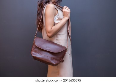 Woman carries brown leather messenger bag in the hand. Unisex bag for sale.