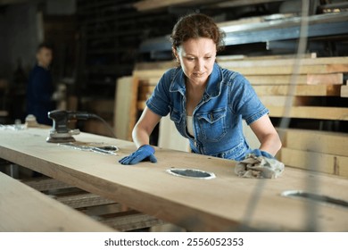 Woman carries out preparatory work with wooden board, grinds surface with hand-held device and levels surface of material - Powered by Shutterstock