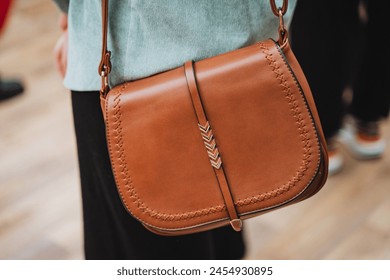 A woman is carrying a brown leather shoulder bag. The bag complements her electric blue sleeve and eyewear, adding a touch of sophistication to her travel outfit