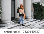 Woman carrying festive gift bag and evergreen plant on snowy winter day, embracing sustainable holiday shopping and eco-friendly gift-giving trends. Outdoor winter fashion, sustainable lifestyle.