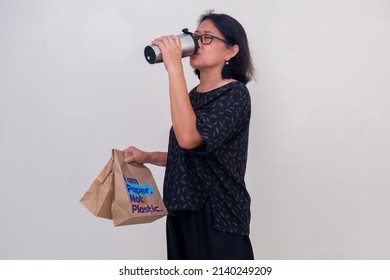 A Woman Carrying Food In Paper Bags And Drinking From Her Tumbler.