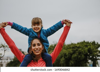 Woman carrying a girl on her shoulder outdoors. Small girl sitting on shoulder of her nanny and smiling.