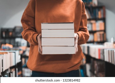 Woman Carrying A Pile Of Books At Bookstore. Close View Of Book Stack Held By A Young Student Girl In The Library. Reading As A Passion.