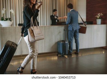 Woman carrying suitcase and talking on mobile phone in a hotel lobby. Traveler female walking with her luggage in hotel hallway. - Shutterstock ID 1040453713
