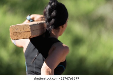 Woman carrying wooden log in a test of the race. Mud race runners, extreme obstacle race. Focused on the log - Powered by Shutterstock