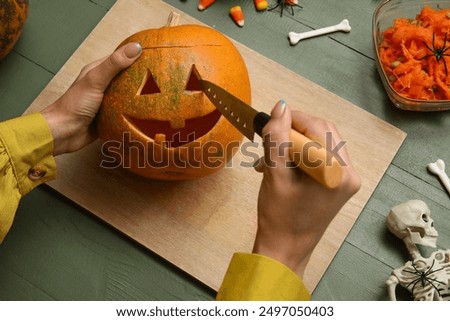 Woman carving Halloween pumpkin at green wooden table